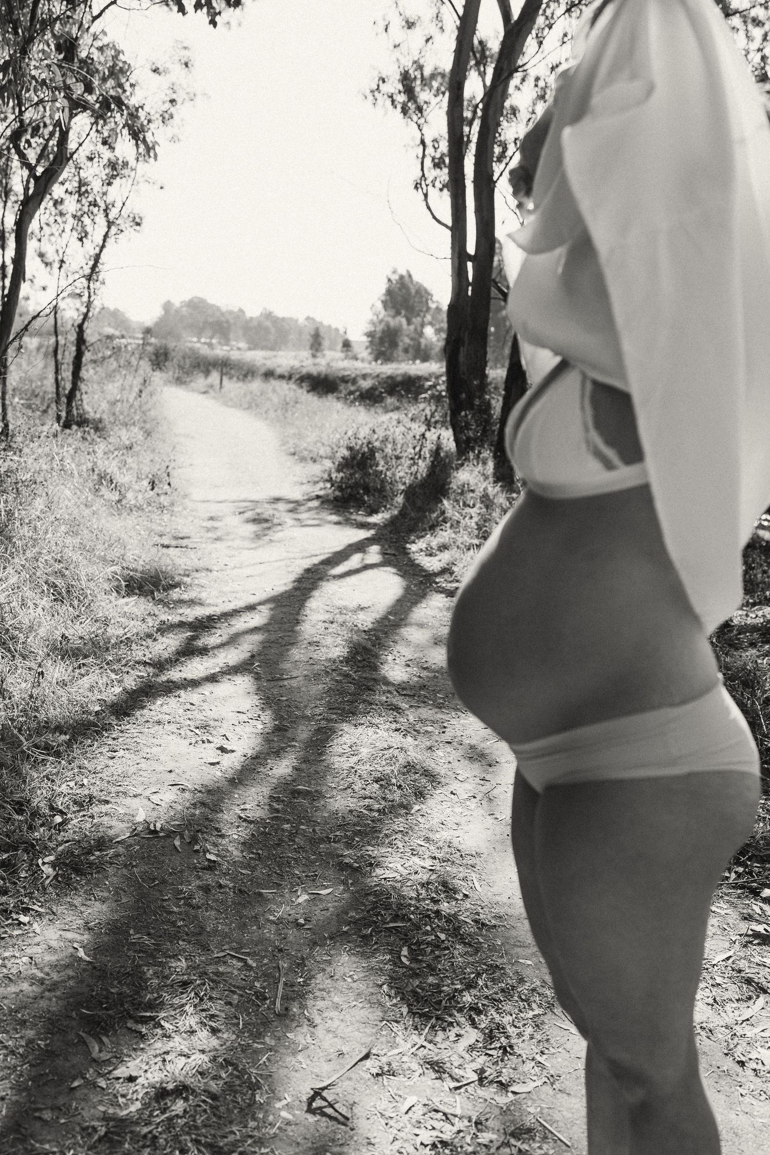 Silhouetted maternity figure walking along a sunlit nature trail.
