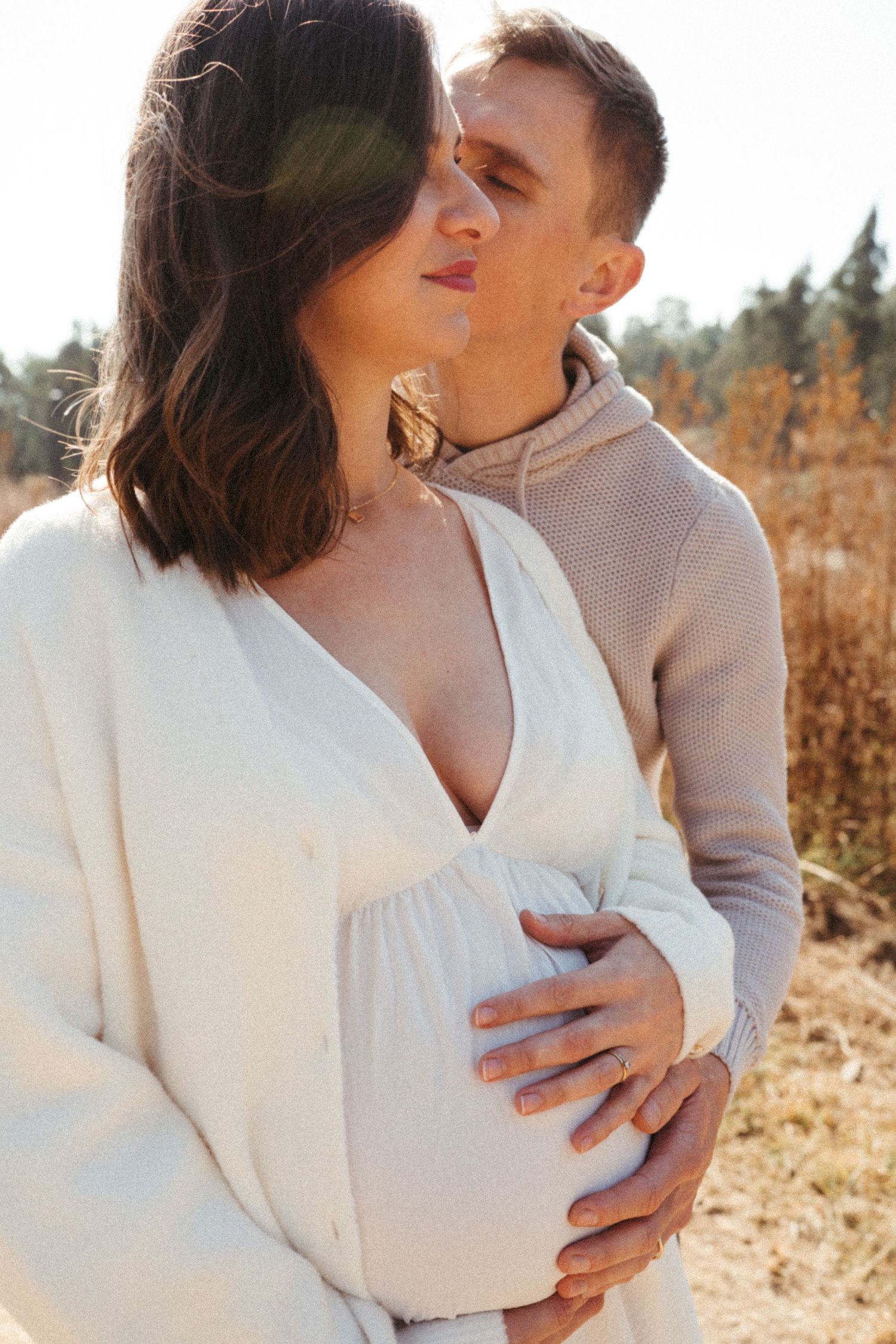Intimate maternity moment captured in warm natural lighting with white sweater.