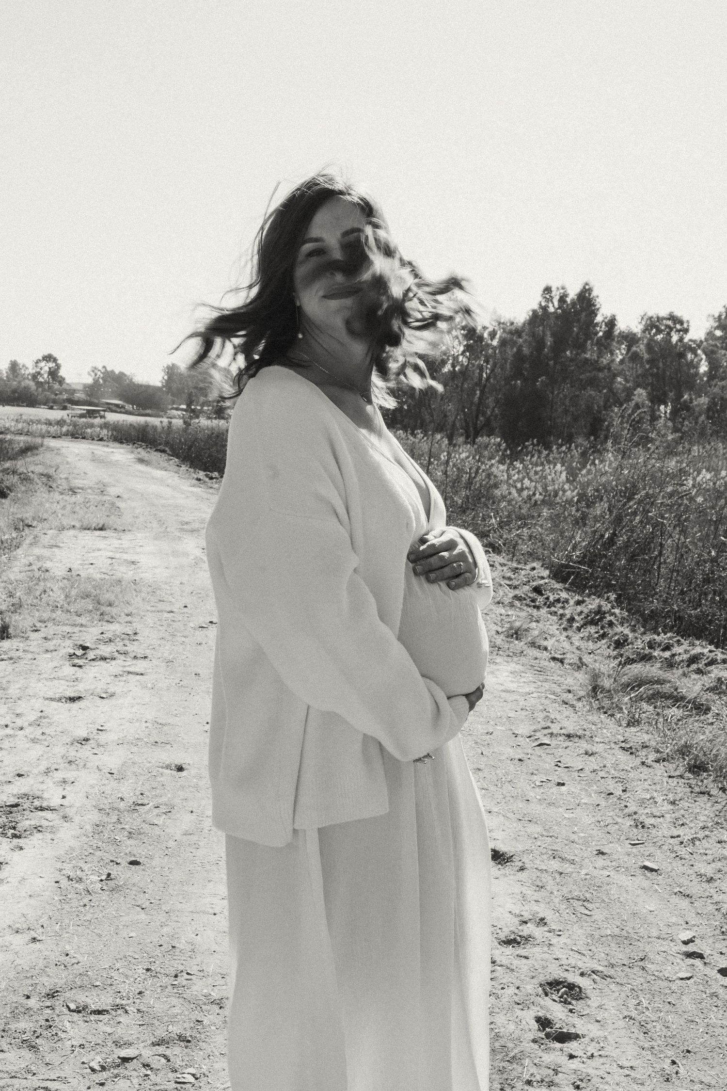 Ethereal maternity portrait in flowing white dress on a rural path.