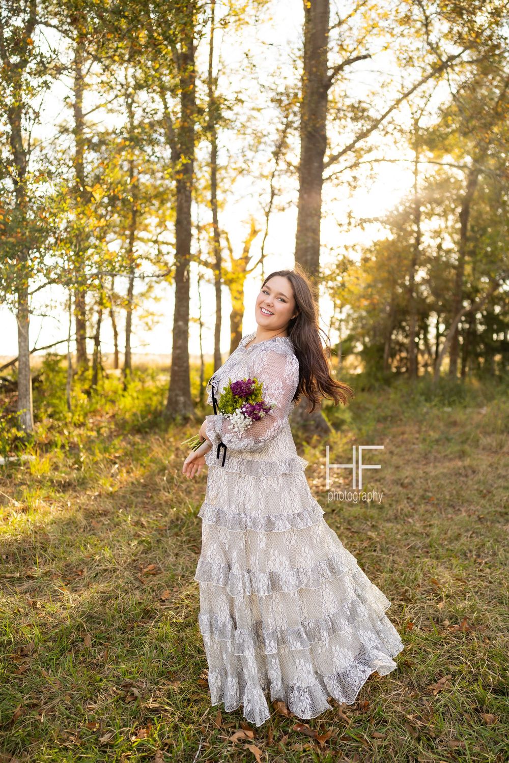 A whimsical forest photoshoot featuring a tiered lace dress and purple wildflower bouquet.