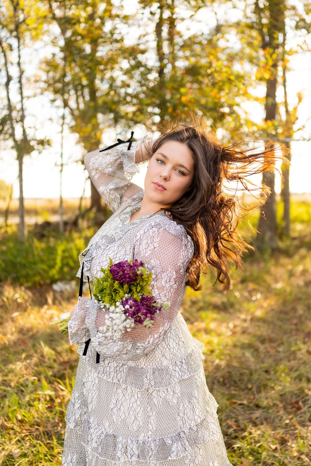 An ethereal outdoor portrait with flowing hair and purple flowers against autumn sunlight.