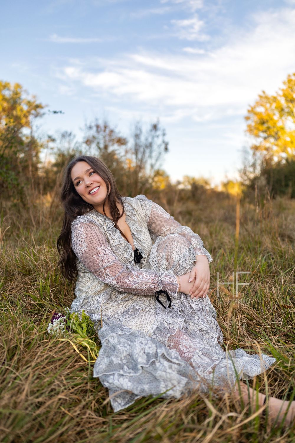 A relaxed outdoor portrait in tall grass featuring an intricate white lace gown.