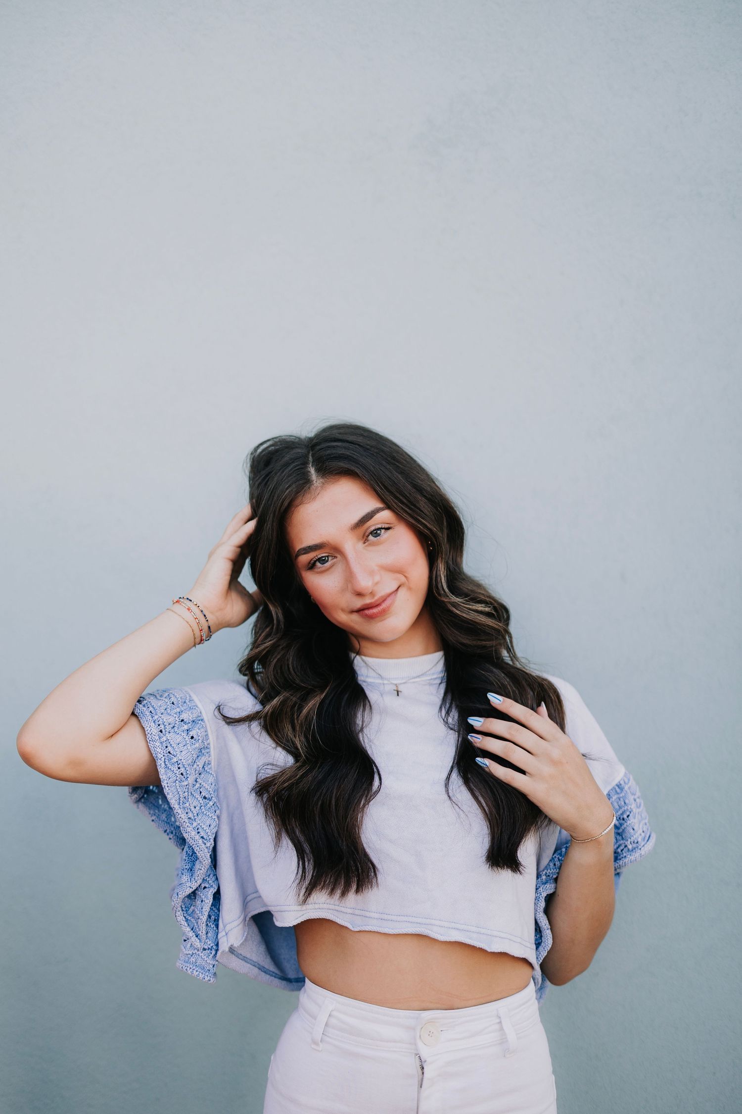 Woman in white crop top and blue ruffled sleeves poses against light blue background.