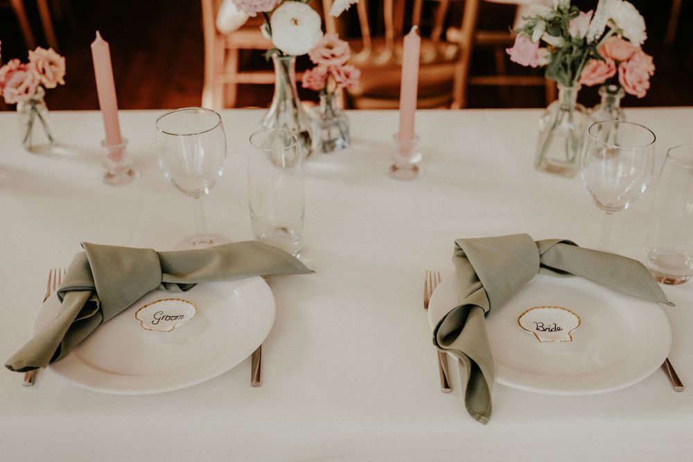 Elegant wedding reception table setting with white floral centerpieces, crystal glasses and pink taper candles.