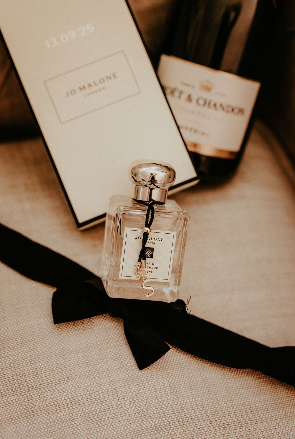 A luxury perfume bottle sits elegantly among black ribbons and white cards in a moody sepia-toned composition.