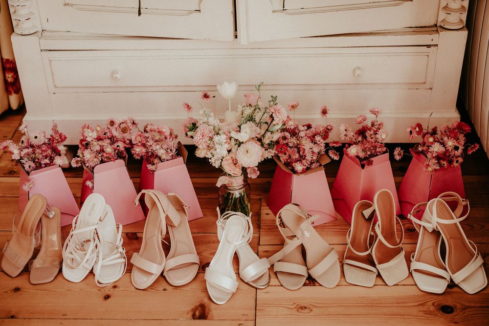 Pink and white bridal party sandals lined up against a wooden wall with delicate floral decorations.