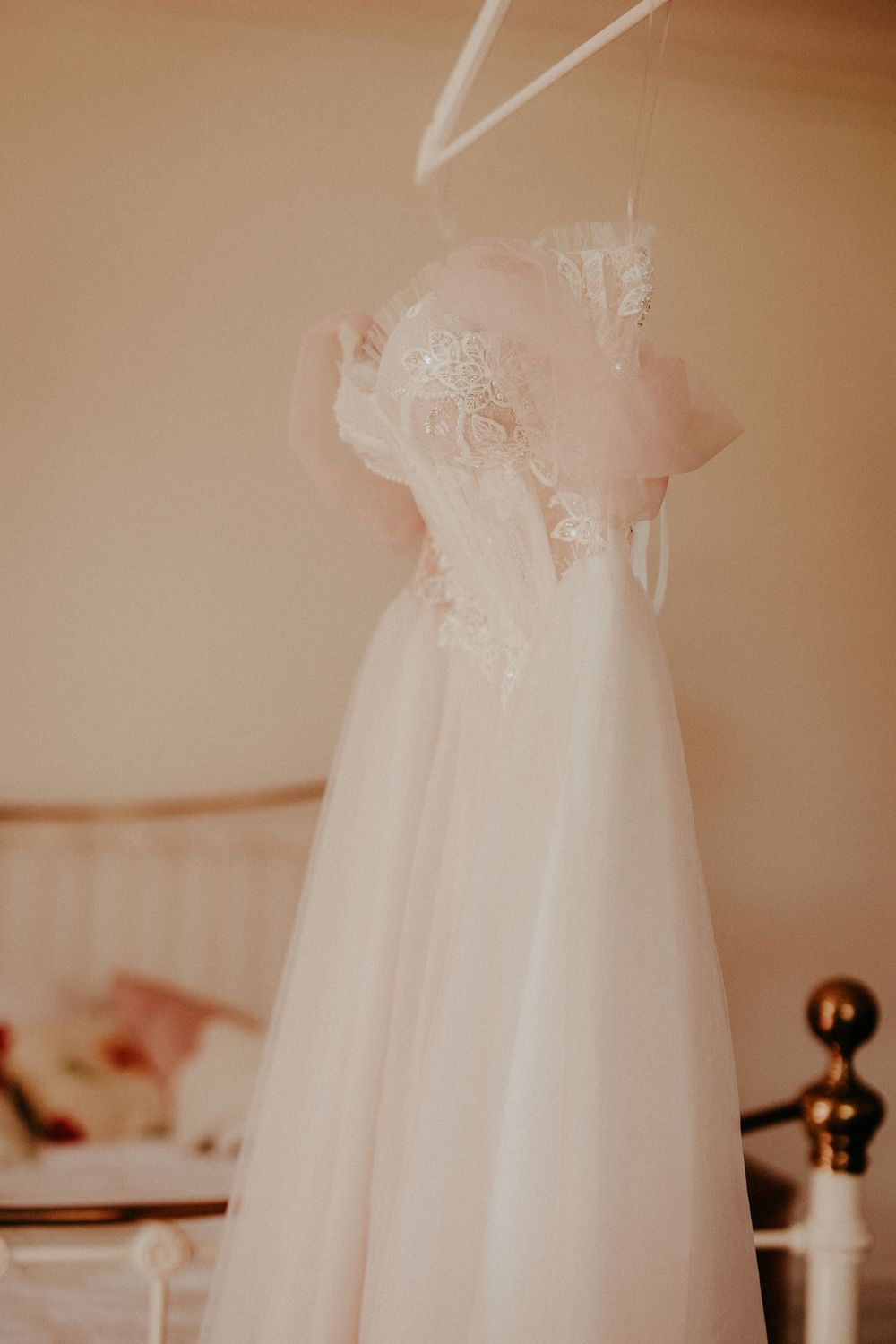 A delicate white christening or baptism dress hangs elegantly against a soft beige background.