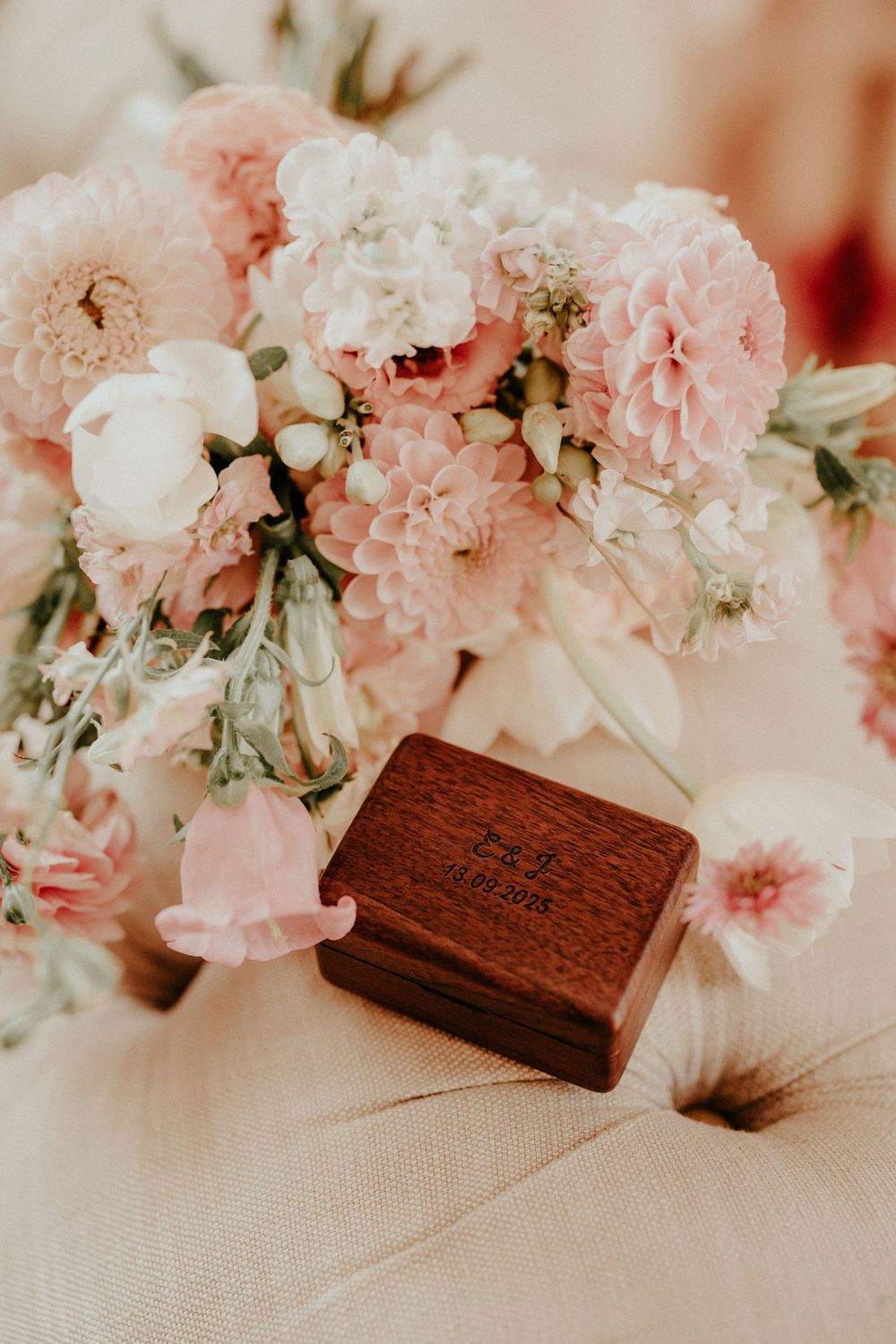Pink and white carnations arranged beside a wooden box on a textured cream surface.