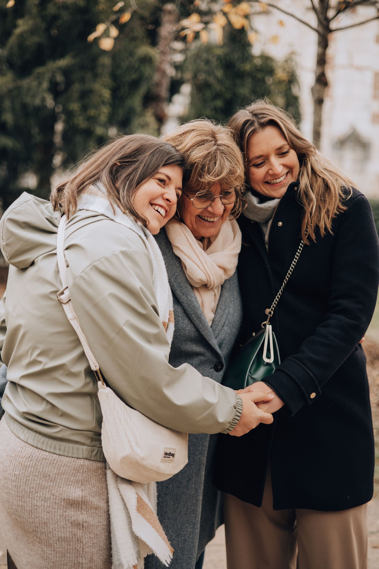 Two daughters embrace their mother warmly outdoors in a tree-lined street in Toulouse, France.