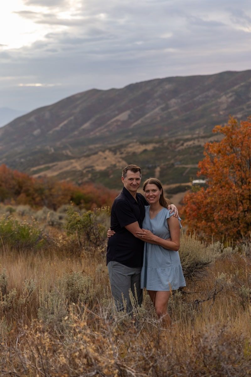 Couple enjoying autumn scenery with mountain backdrop and fall foliage in warm evening light.