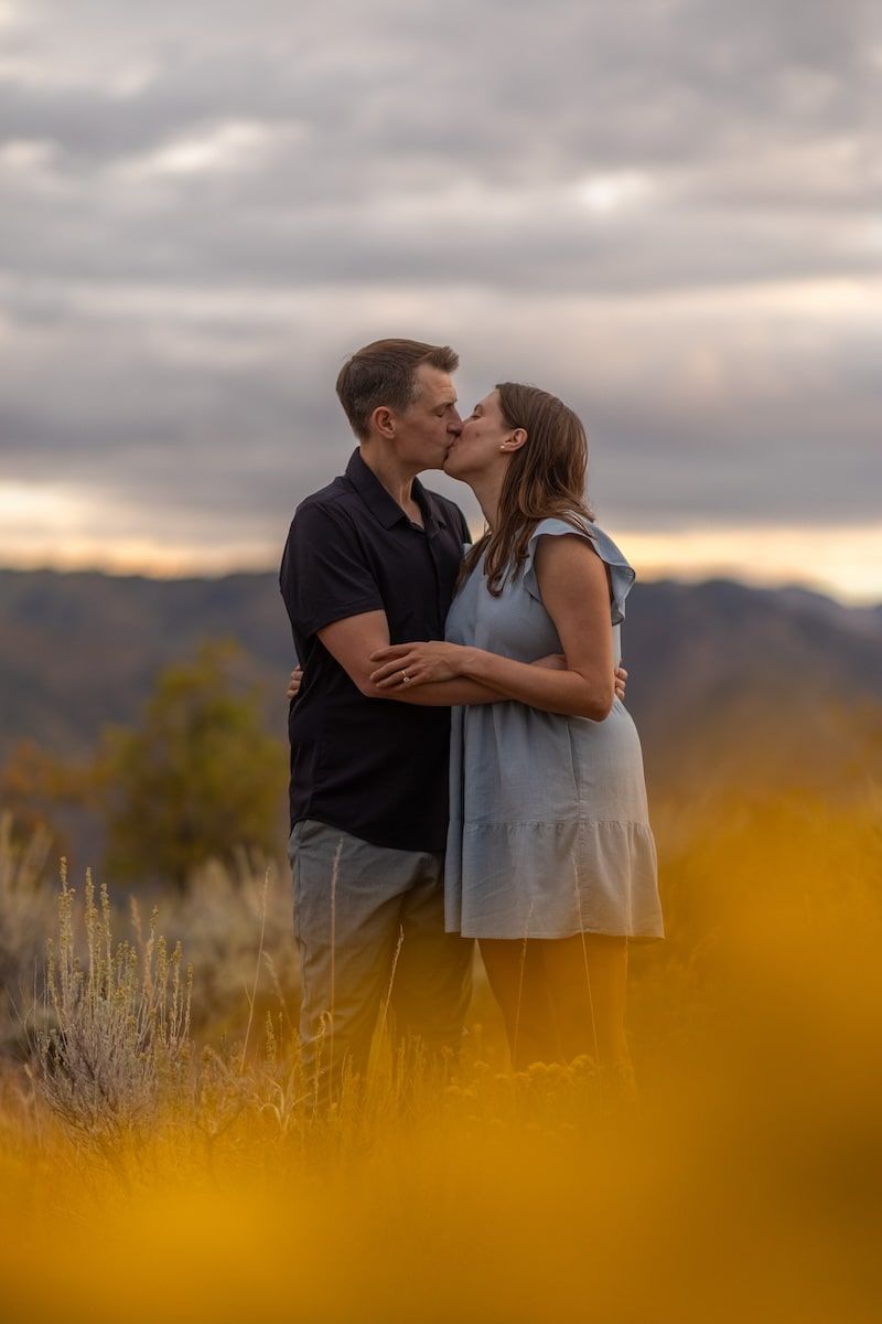 A romantic couple shares a tender moment at sunset in a field with mountains in the background.