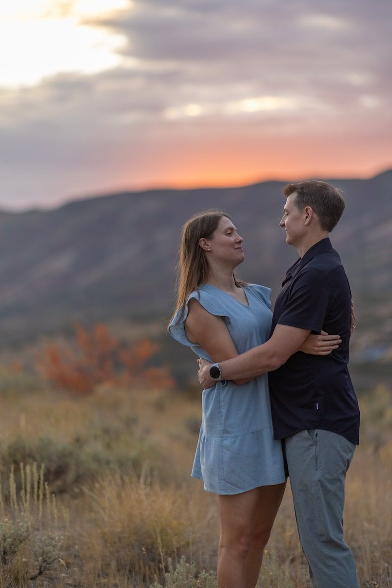 A romantic couple embraces against a scenic mountain backdrop during golden hour sunset.