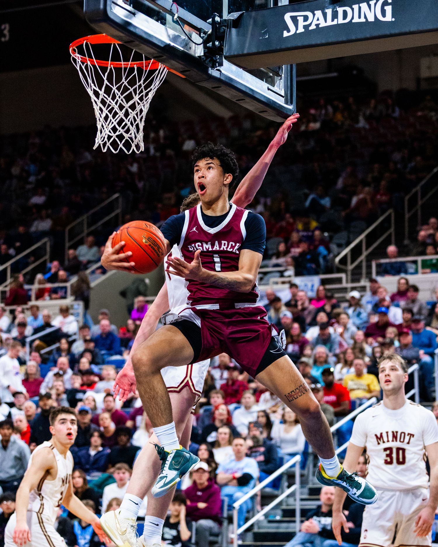 Basketball player in maroon jersey leaps towards the hoop for a layup during an intense game against opposing team.