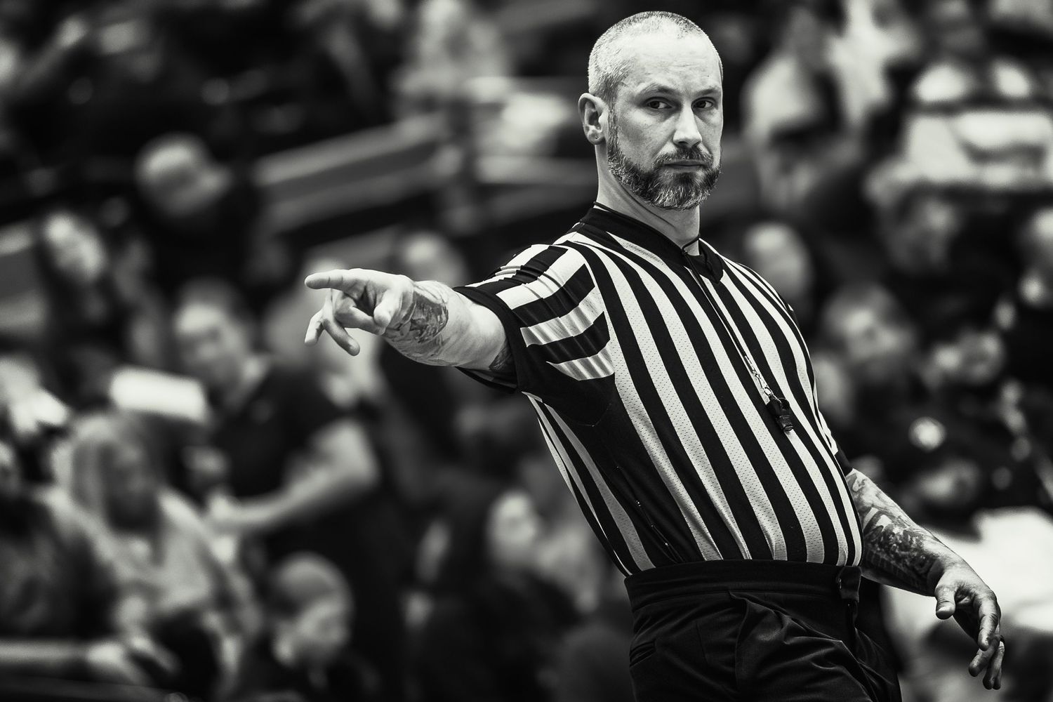 A basketball referee in striped uniform makes a hand signal call during an intense game moment.