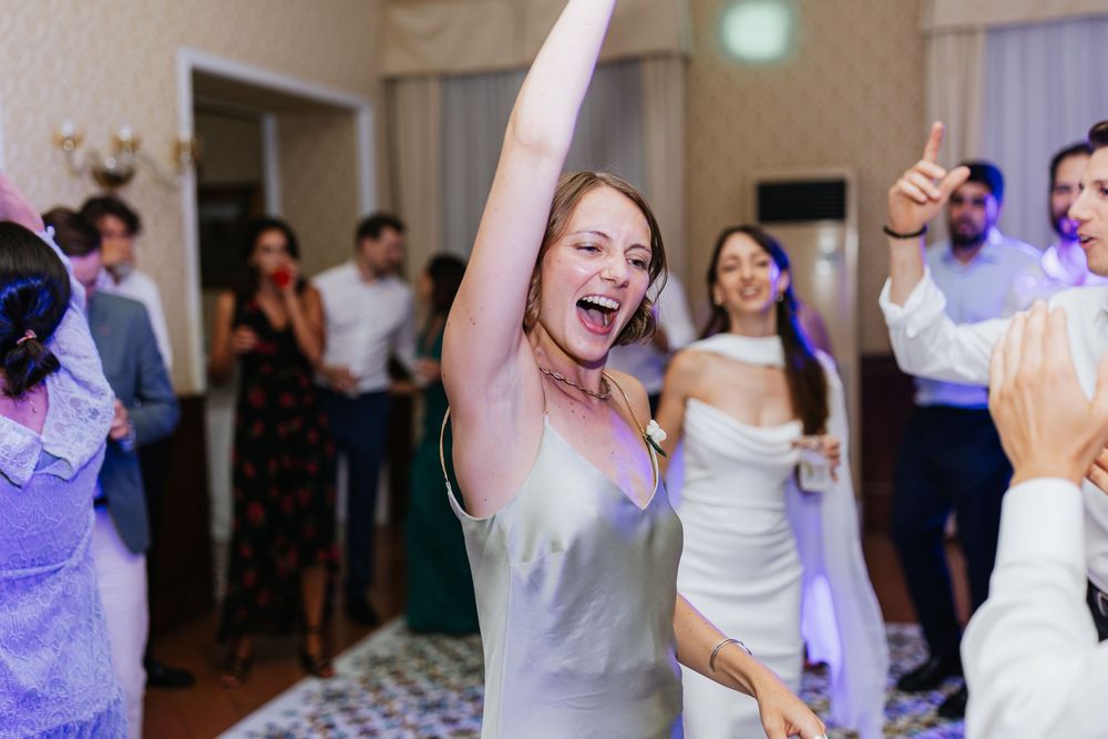 Wedding guests dance and celebrate together on a lively dance floor illuminated with purple lighting at a reception.