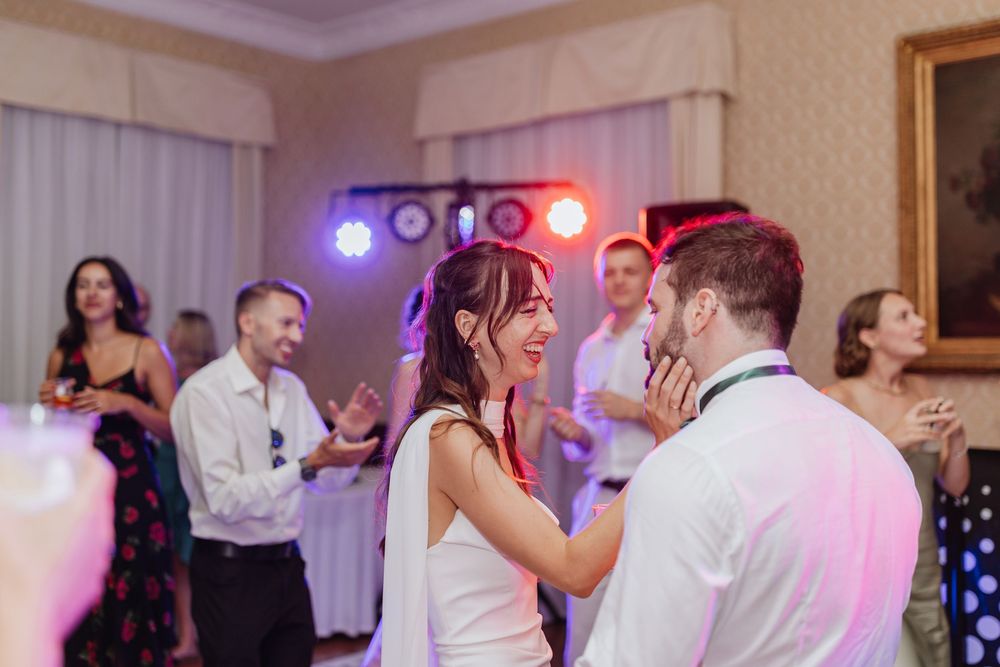 Wedding guests dance together on a reception dance floor illuminated by colorful purple and red lighting.