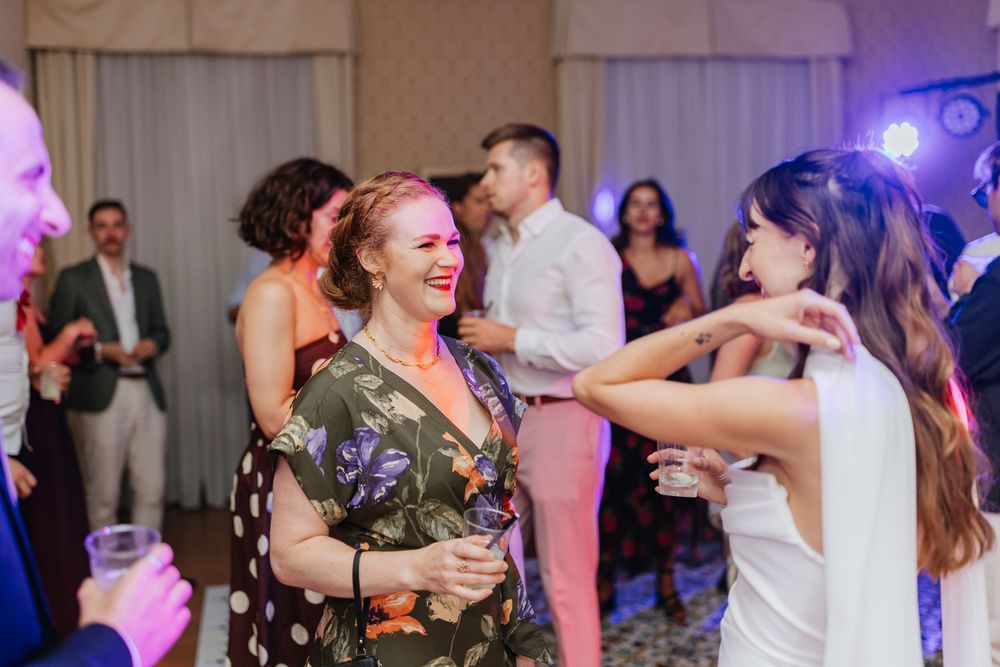 People dancing and laughing together at a wedding reception with colorful lighting and party atmosphere.