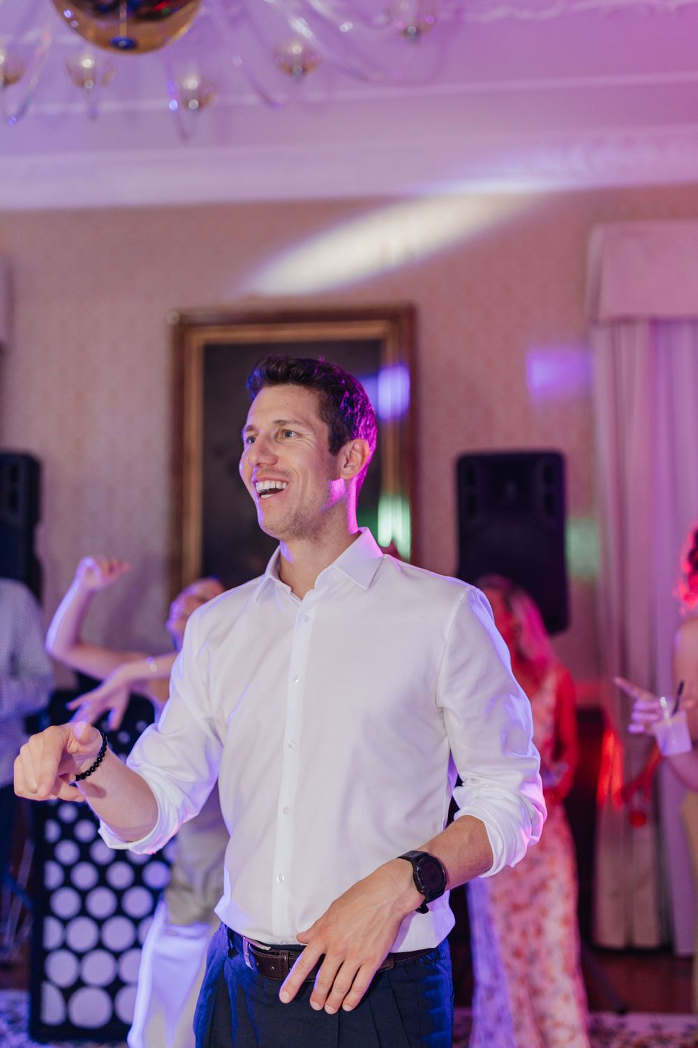A joyful dancer in a white button-down shirt moves energetically on a dance floor with purple lighting.