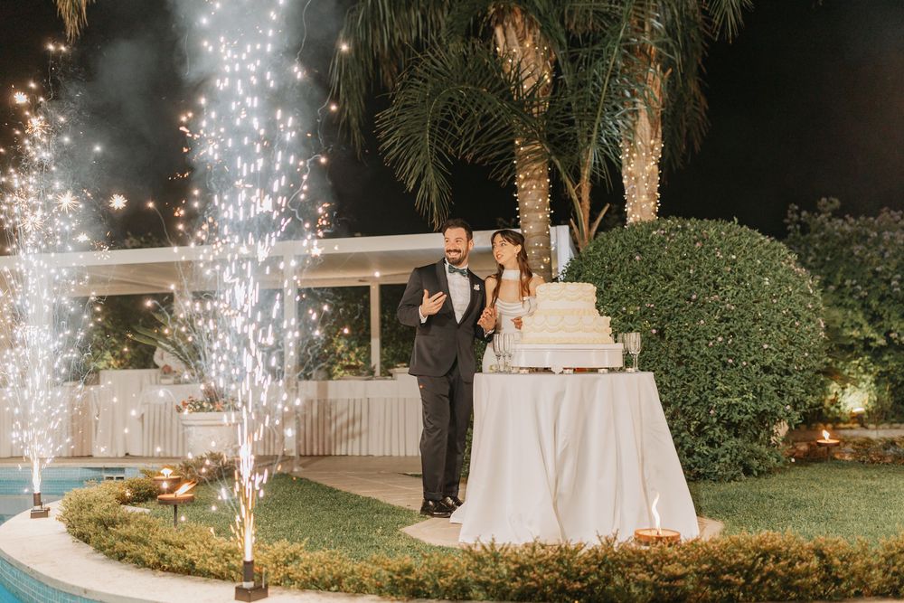 A wedding celebration at night with sparklers illuminating an outdoor garden setting near a tiered white cake.