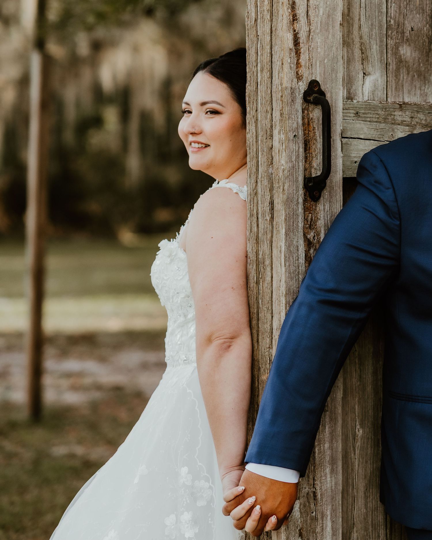 Rustic wedding portrait with couple posing against wooden post in natural outdoor setting.
