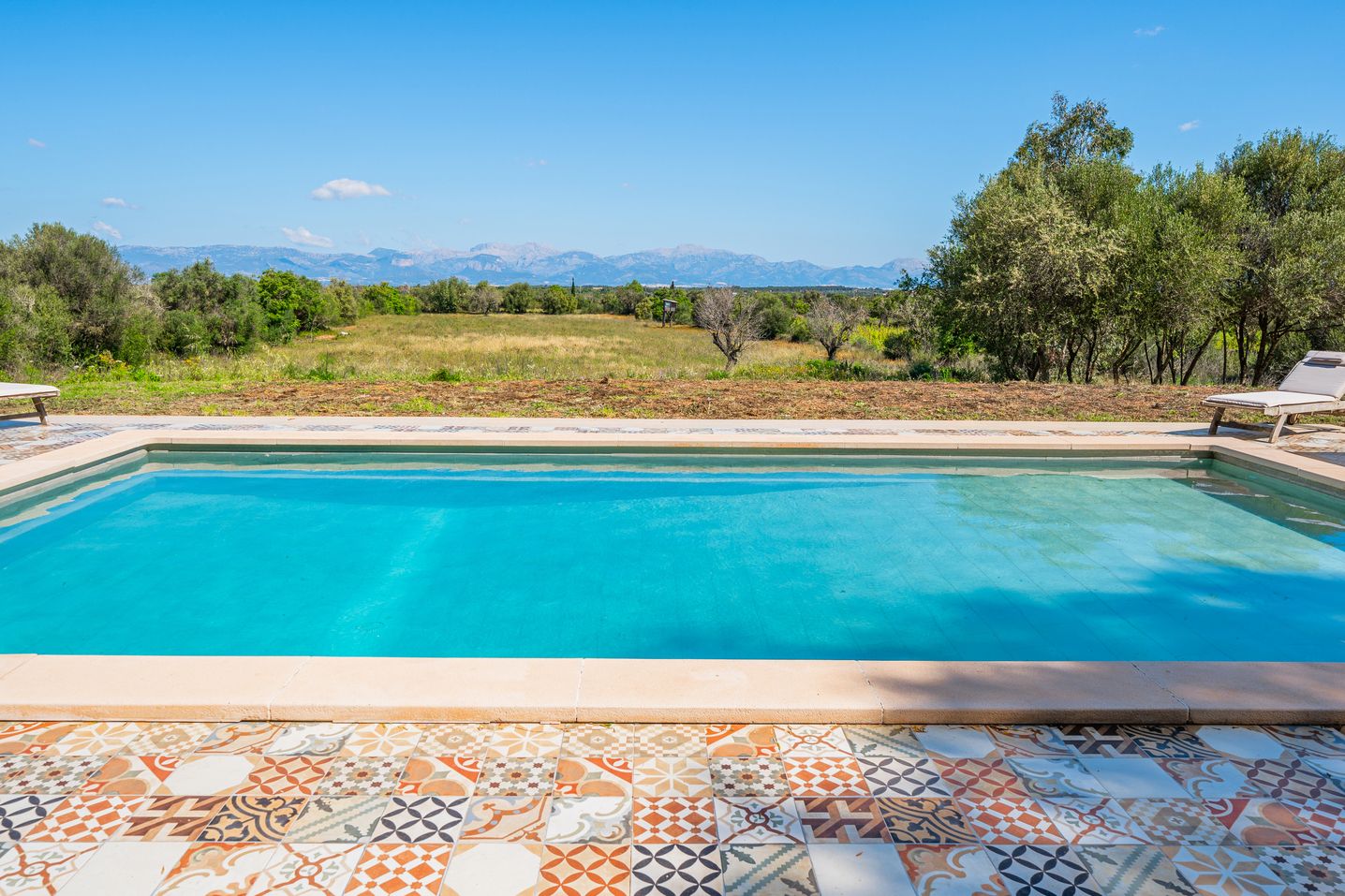 Infinity pool with crystal clear water overlooking a scenic mountain landscape on a bright sunny day.