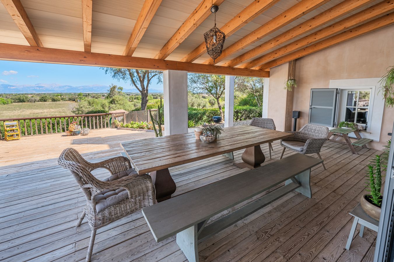Spacious covered deck with rustic wooden dining table and chairs overlooking a scenic mountain landscape view.