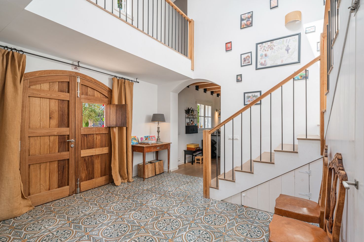 Bright entryway with wooden staircase, patterned tile floor, and rustic wooden door features decorative wall art.