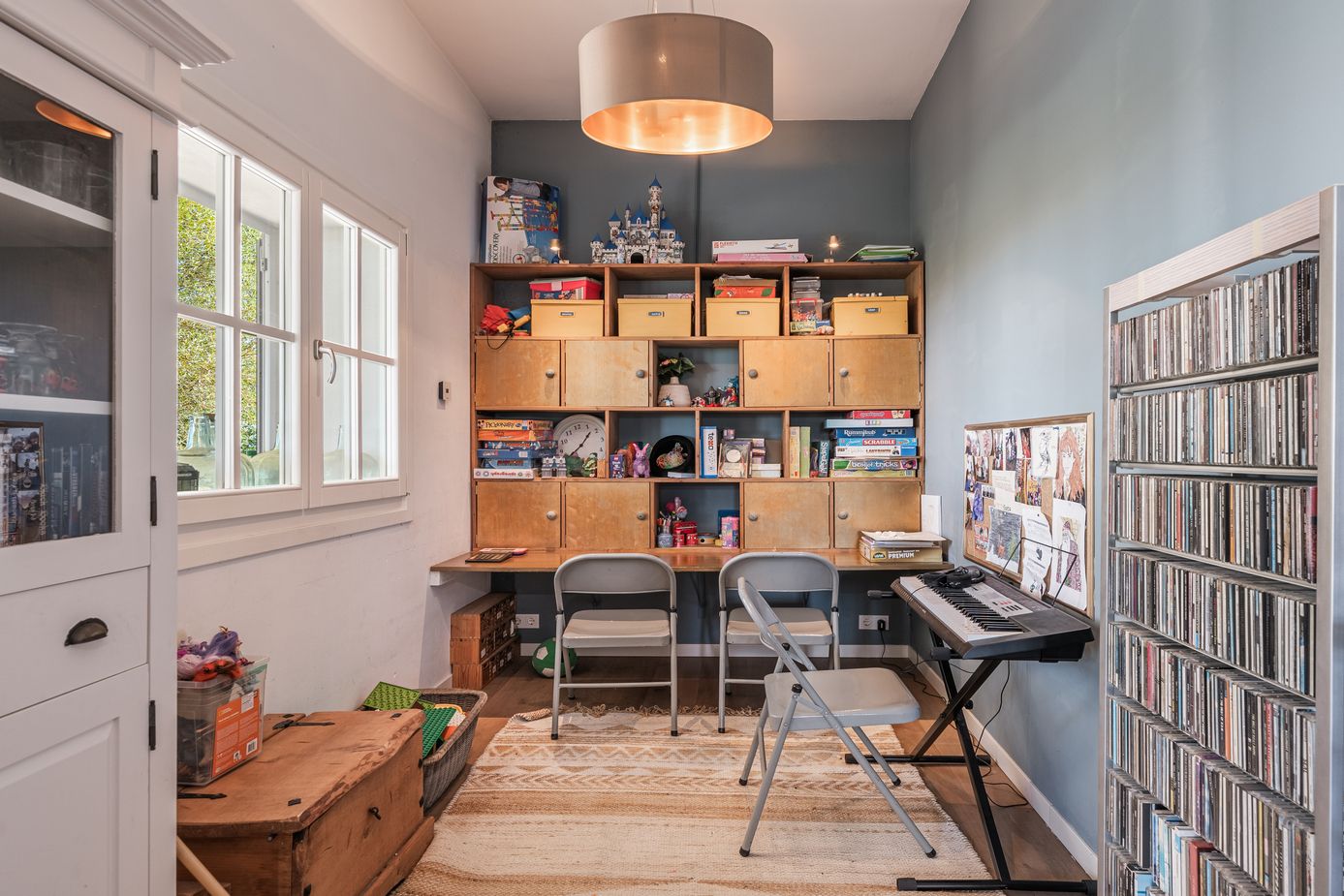 A cozy home office with wooden shelving, music keyboard, and large CD collection displayed on wall-mounted shelves.