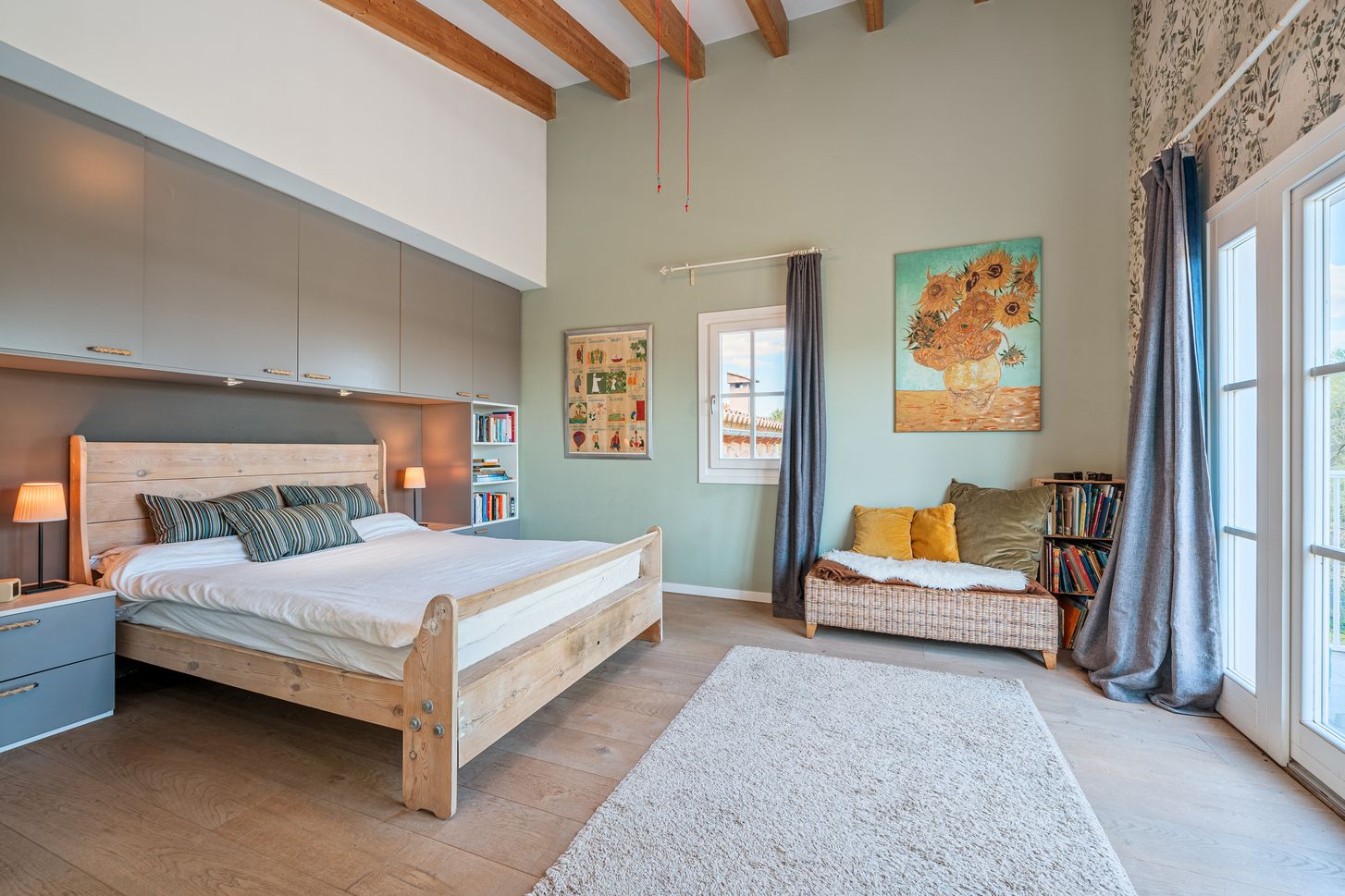 Modern loft bedroom with exposed wooden beams, white walls, and large windows letting in natural light.