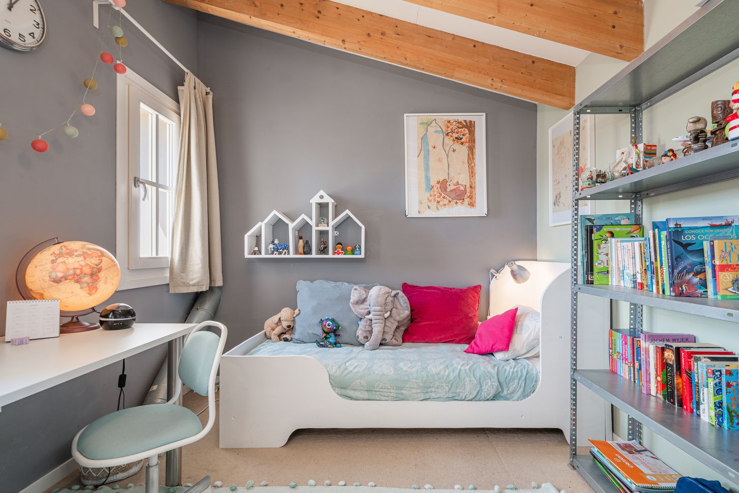 A modern children's bedroom features exposed wooden beams, built-in storage, and colorful decor against gray walls.