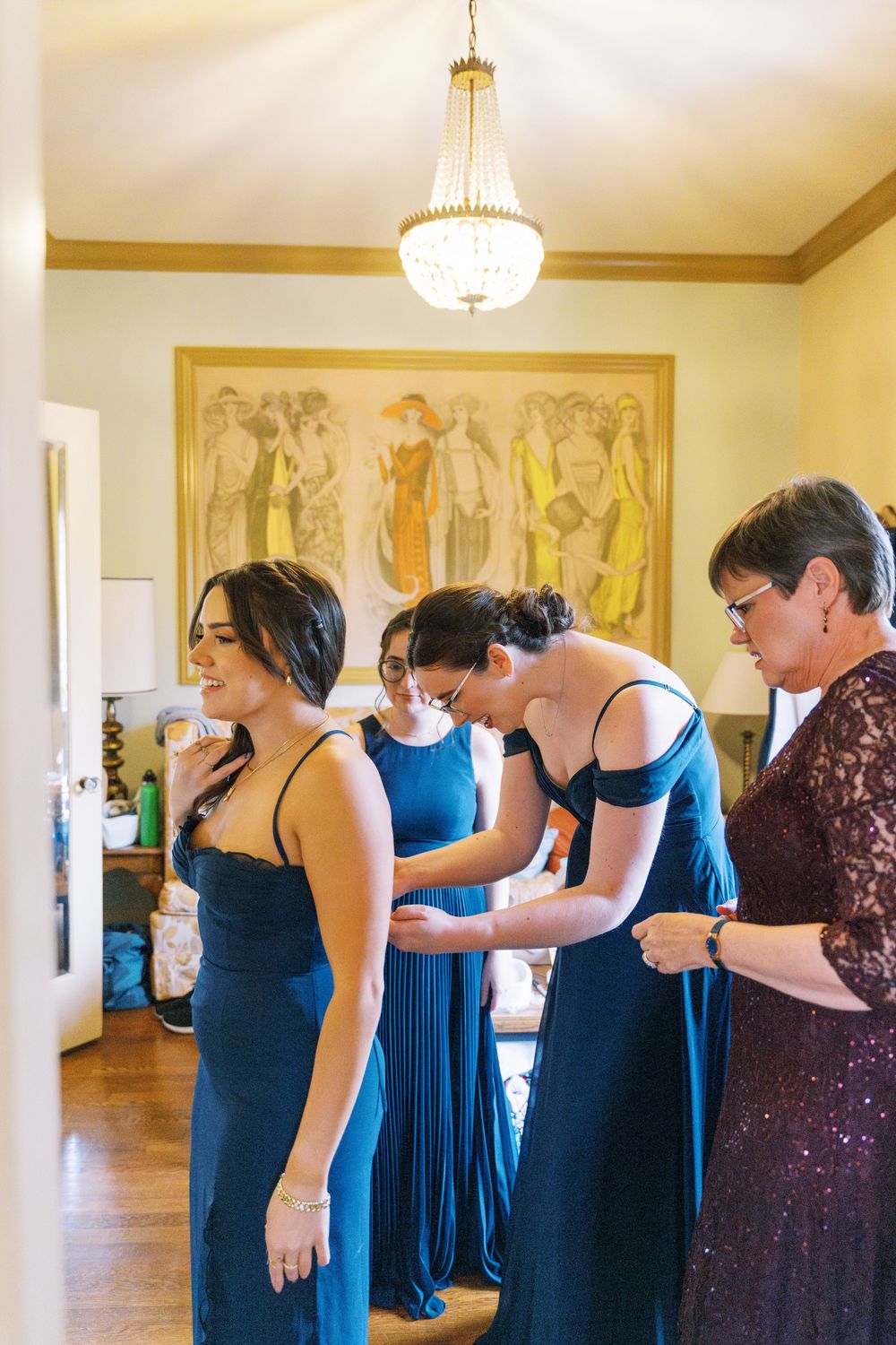Wedding party members in navy blue dresses help with final preparations in an elegant room.
