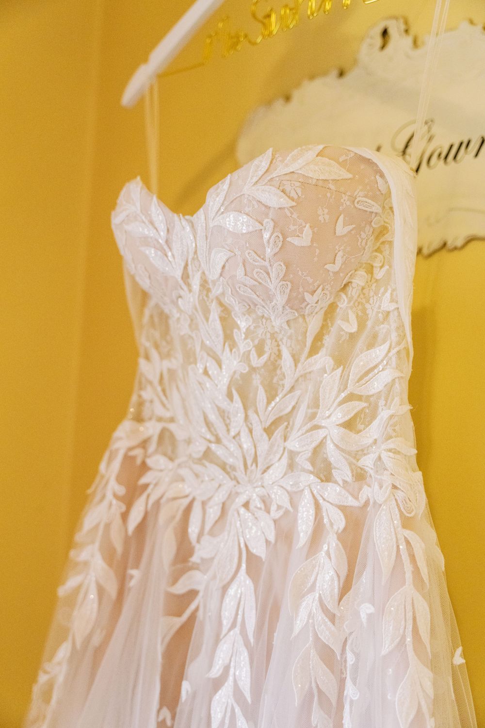 Close-up details of delicate floral lace appliques on a white wedding gown against a golden background.