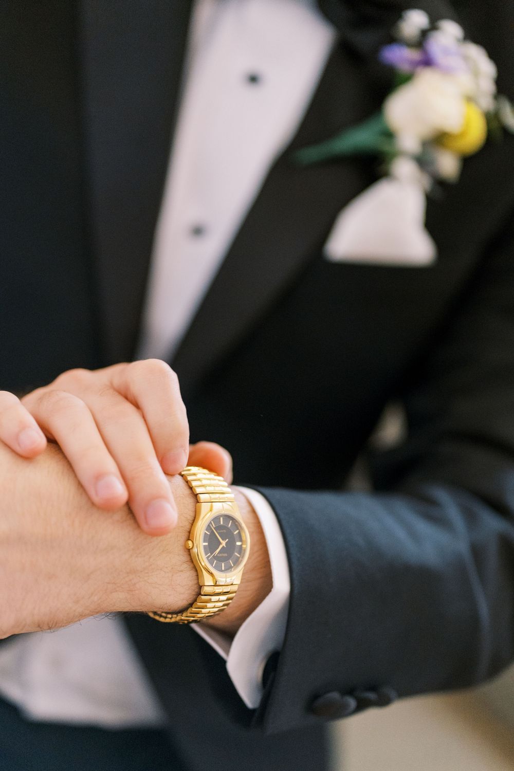 Close-up of gold watch on wrist with black suit sleeve visible.