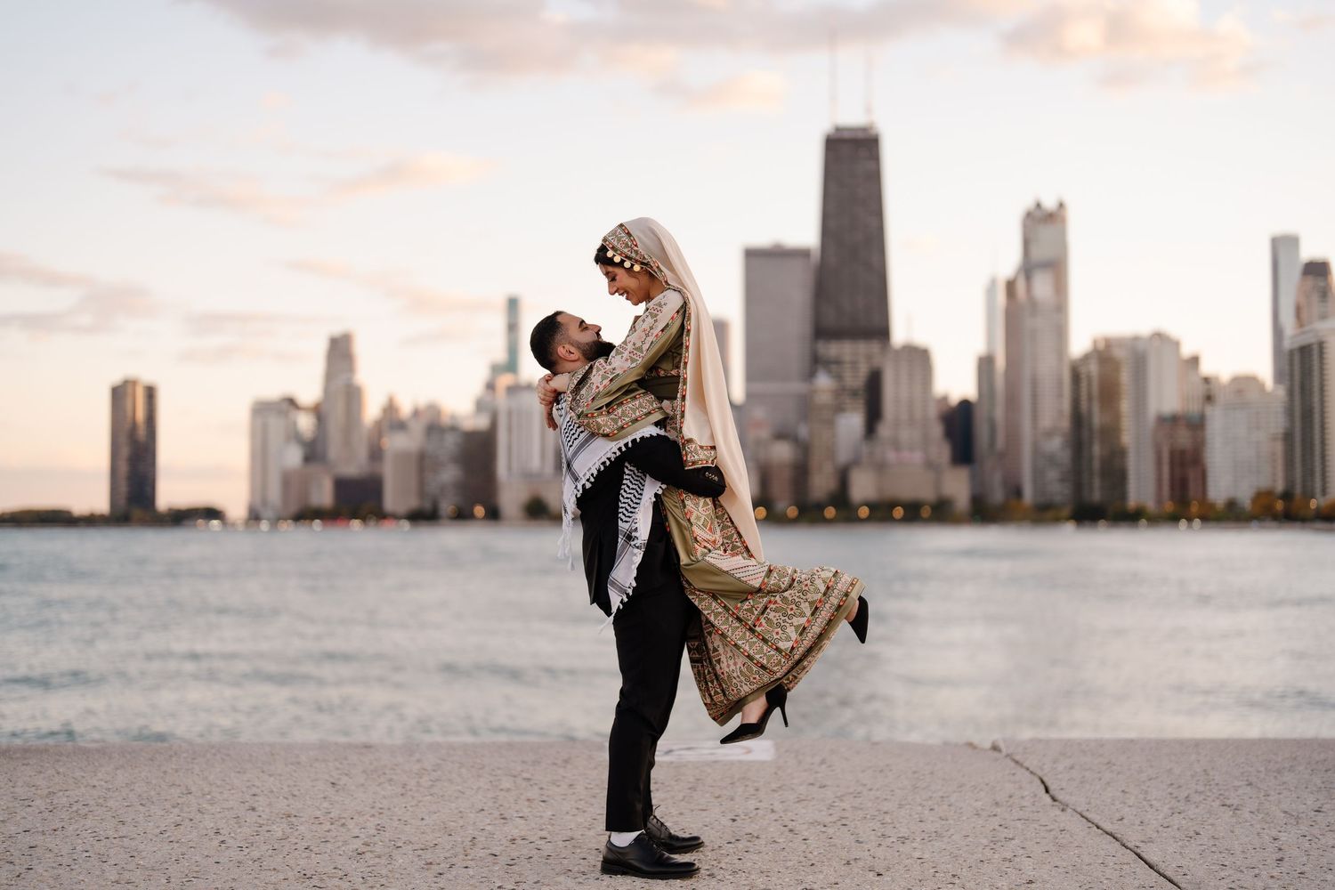 Muslim couple celebrating engagement with lift pose in front of Chicago skyline at sunset.