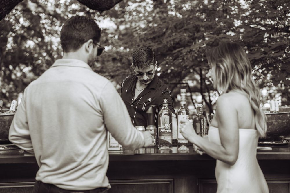 Guests enjoying a wedding reception outdoors under trees at sunset.