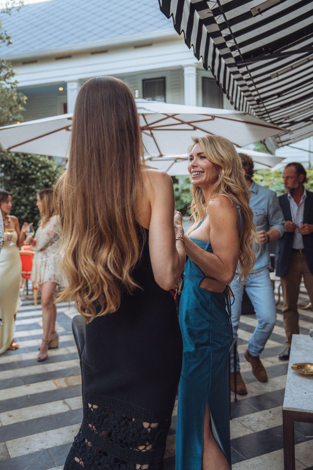 Wedding guests socializing under striped awning at outdoor venue.