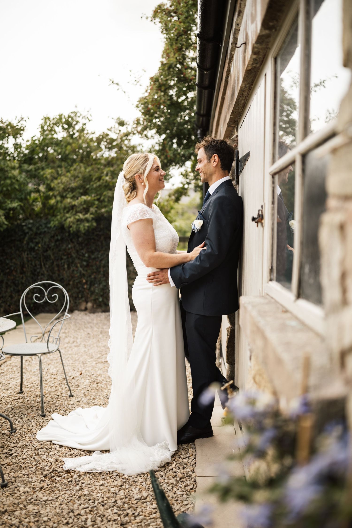 A couple shares a romantic moment in a garden setting with lush trees and flowers during their wedding day.