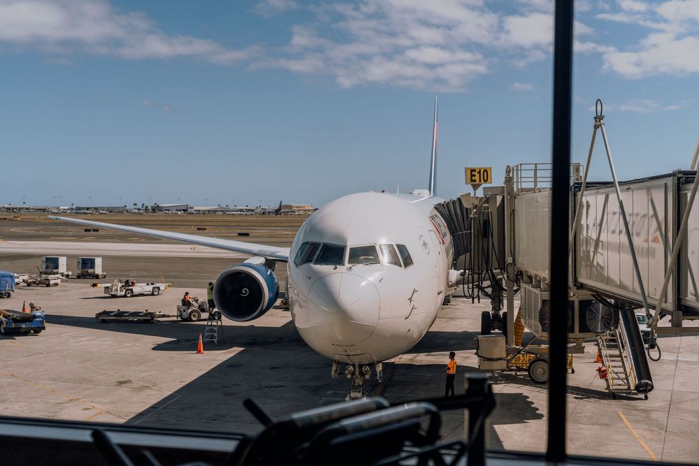 Multiple commercial airplanes parked on airport tarmac under blue sky with mountains in background.