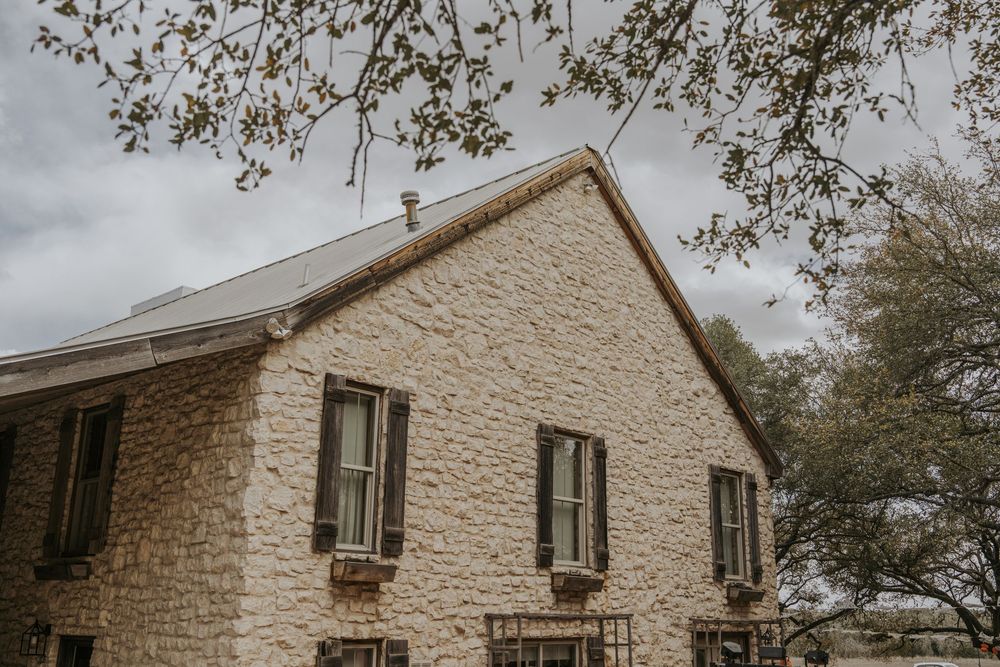Rustic stone wedding venue exterior with overcast sky and trees in background.