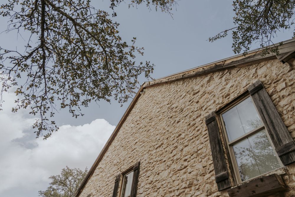 Stone facade of rustic wedding venue with tree branches framing the building.