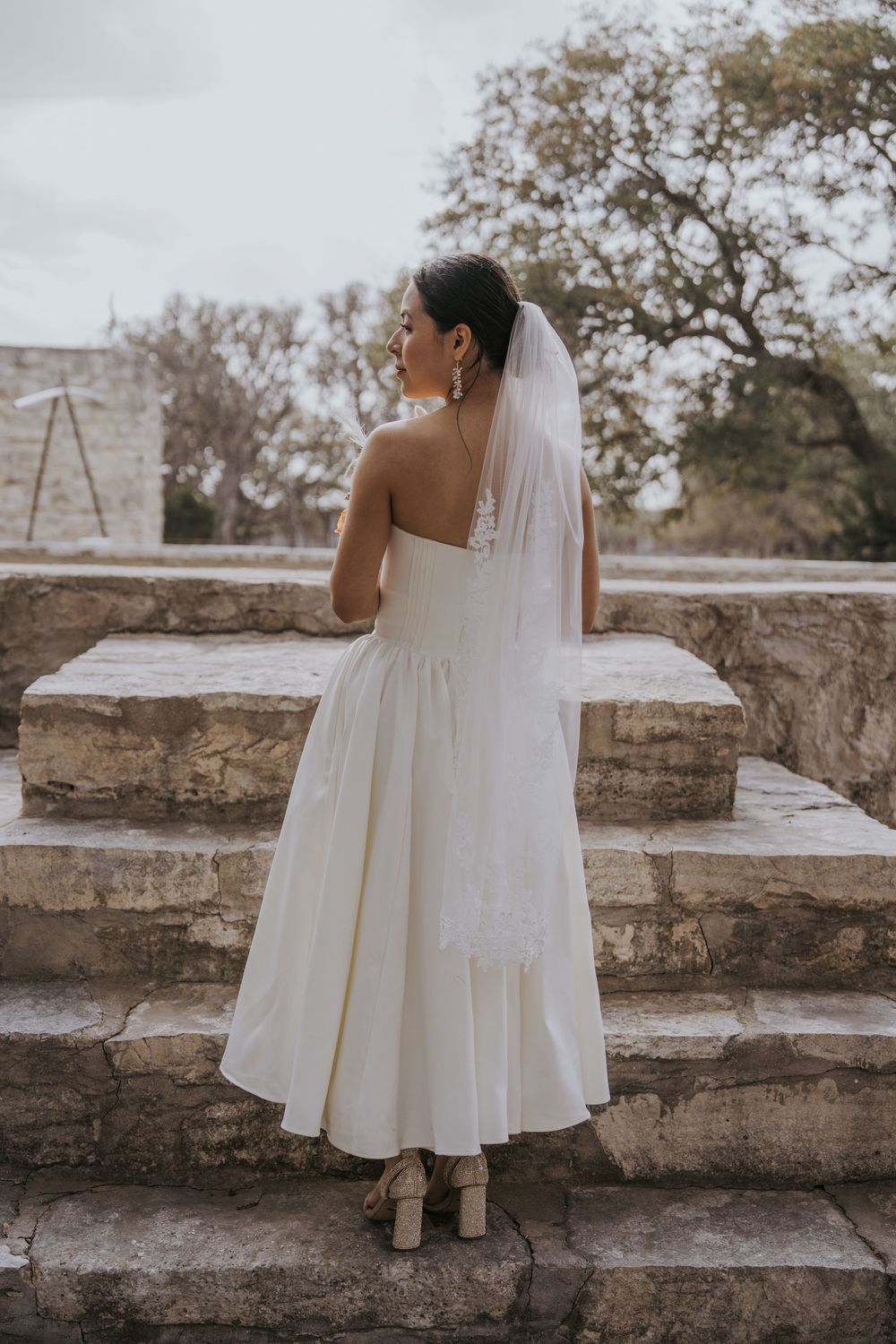 Short white wedding dress and veil photographed on stone steps outdoors.