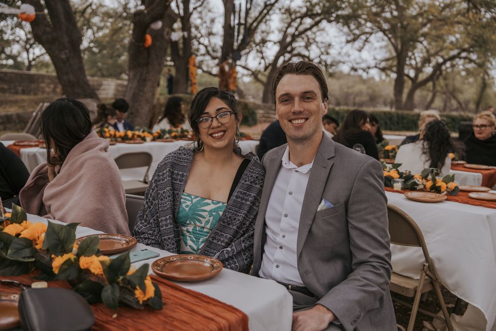 Wedding guests seated at rustic outdoor reception tables decorated with orange floral centerpieces.