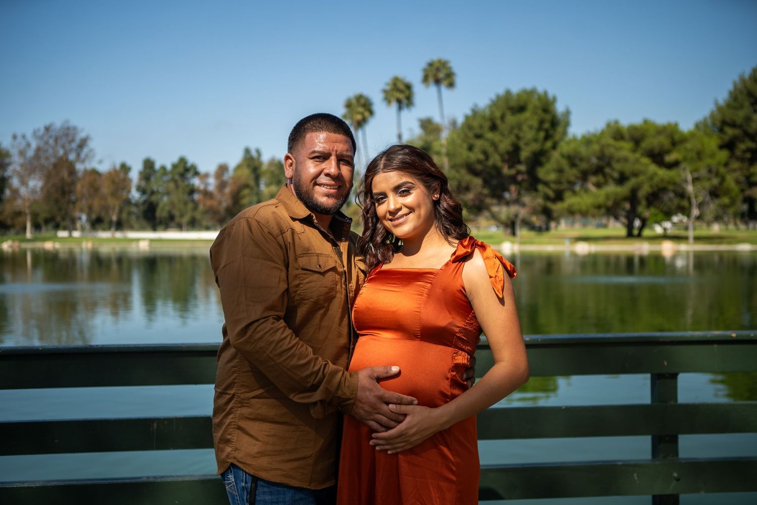 Family poses together by a scenic lake with palm trees and blue skies.
