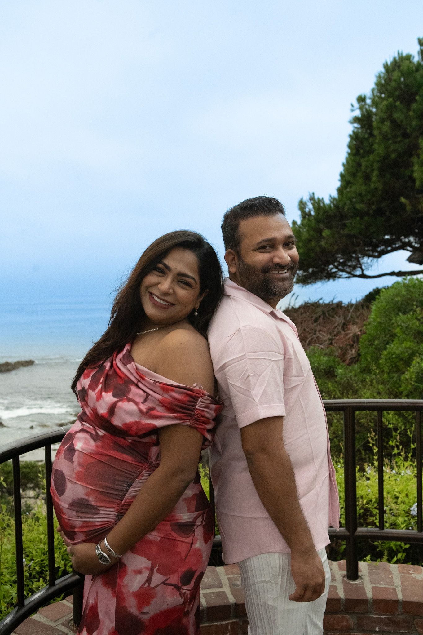 Couple poses together on coastal overlook during maternity photoshoot.