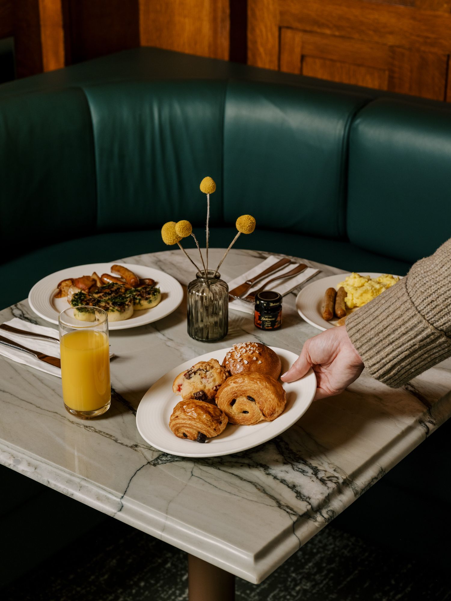 Breakfast spread with pastries and orange juice at a green leather booth.