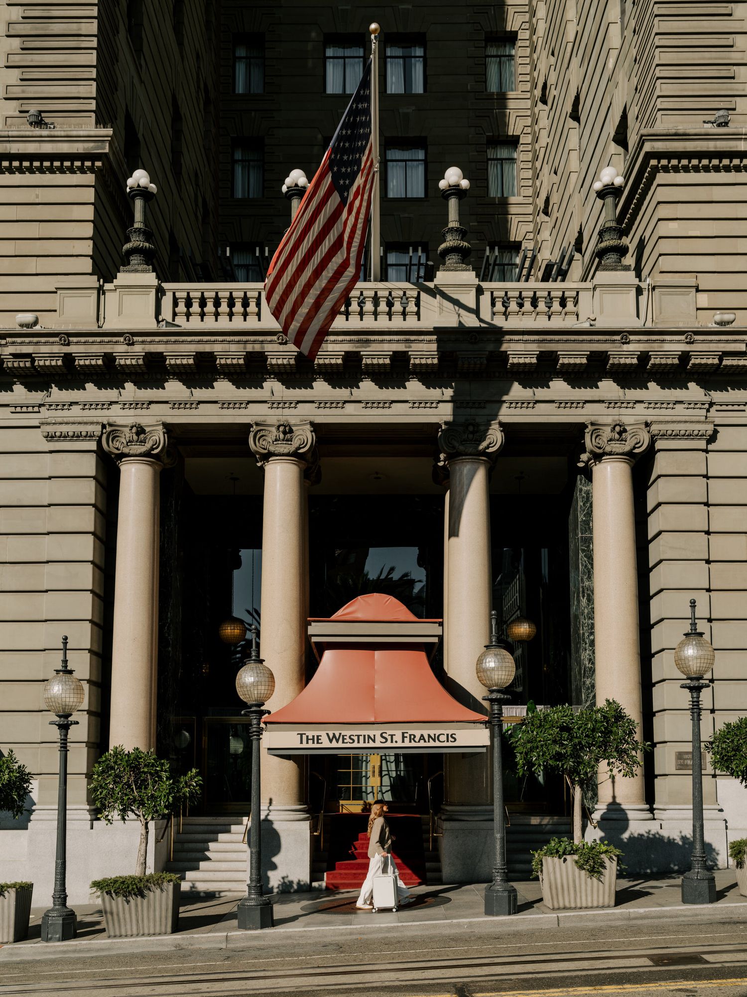 Exterior view of a grand hotel entrance with white columns and American flags displayed on the facade.
