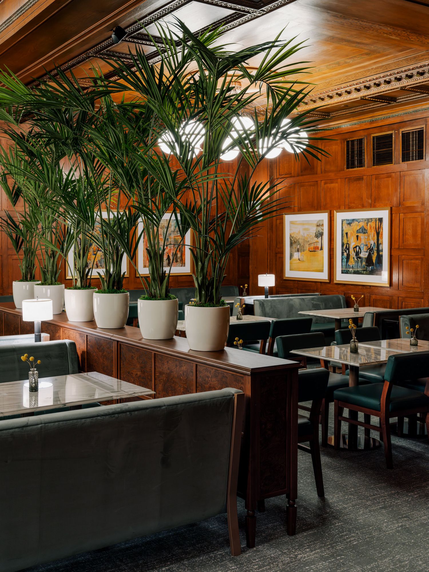 Modern restaurant interior with wooden walls, black leather booths, and potted palm plants creating an elegant ambiance.
