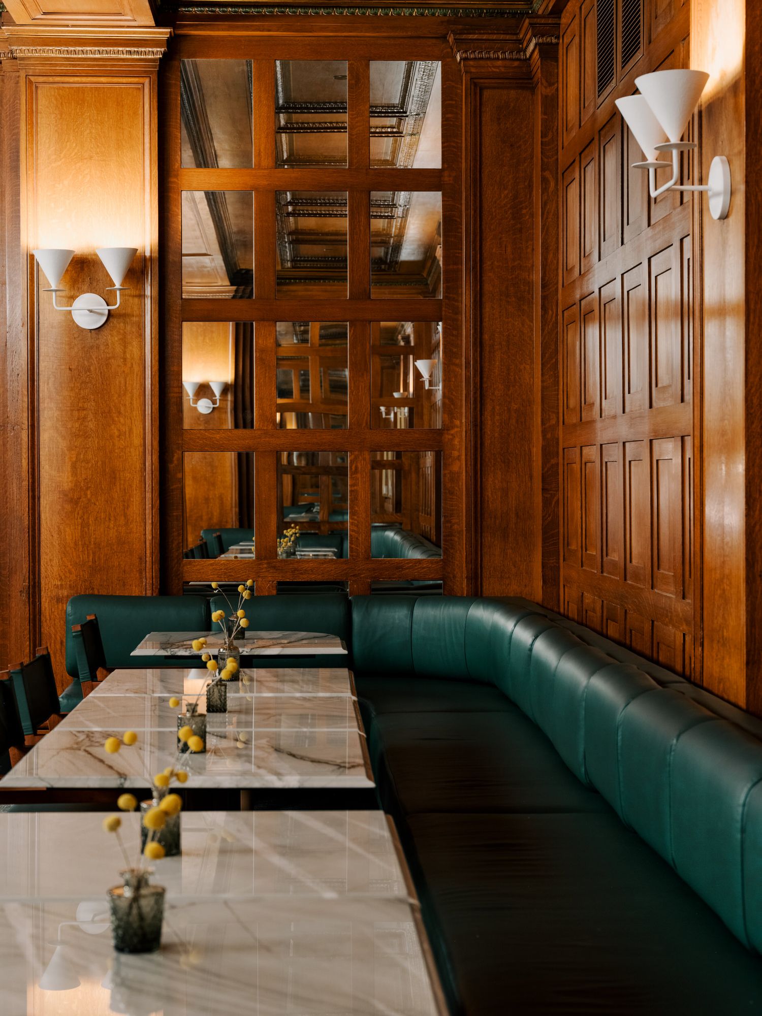 Elegant restaurant interior with wood-paneled walls, green leather banquettes, and white tablecloths set for dining.