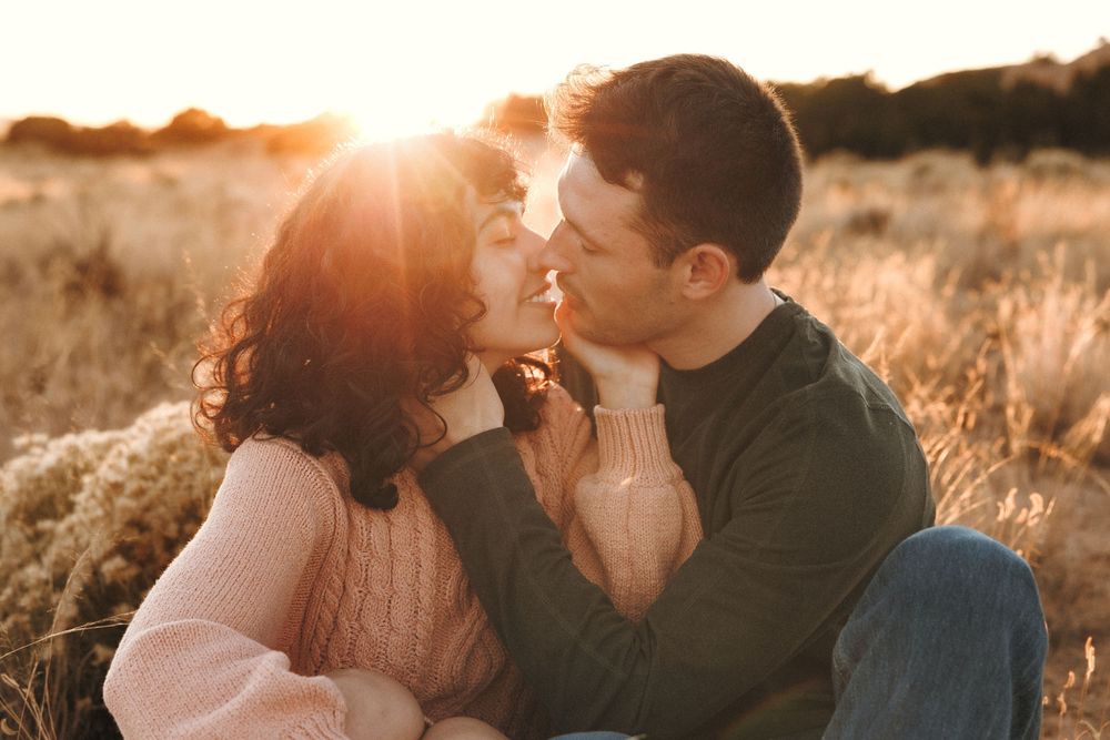 Couple sharing a tender kiss in glowing sunset light surrounded by golden field grass.