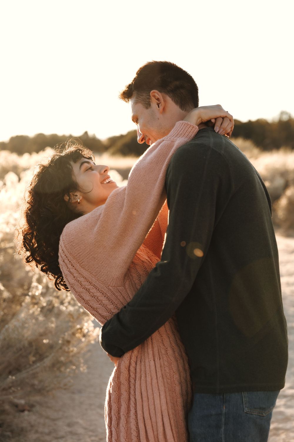 Happy couple embracing and smiling at golden hour on a sunny desert path with warm backlight.